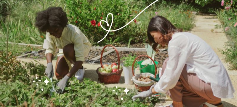 Two people crouch in a garden smiling as they dig in the soil